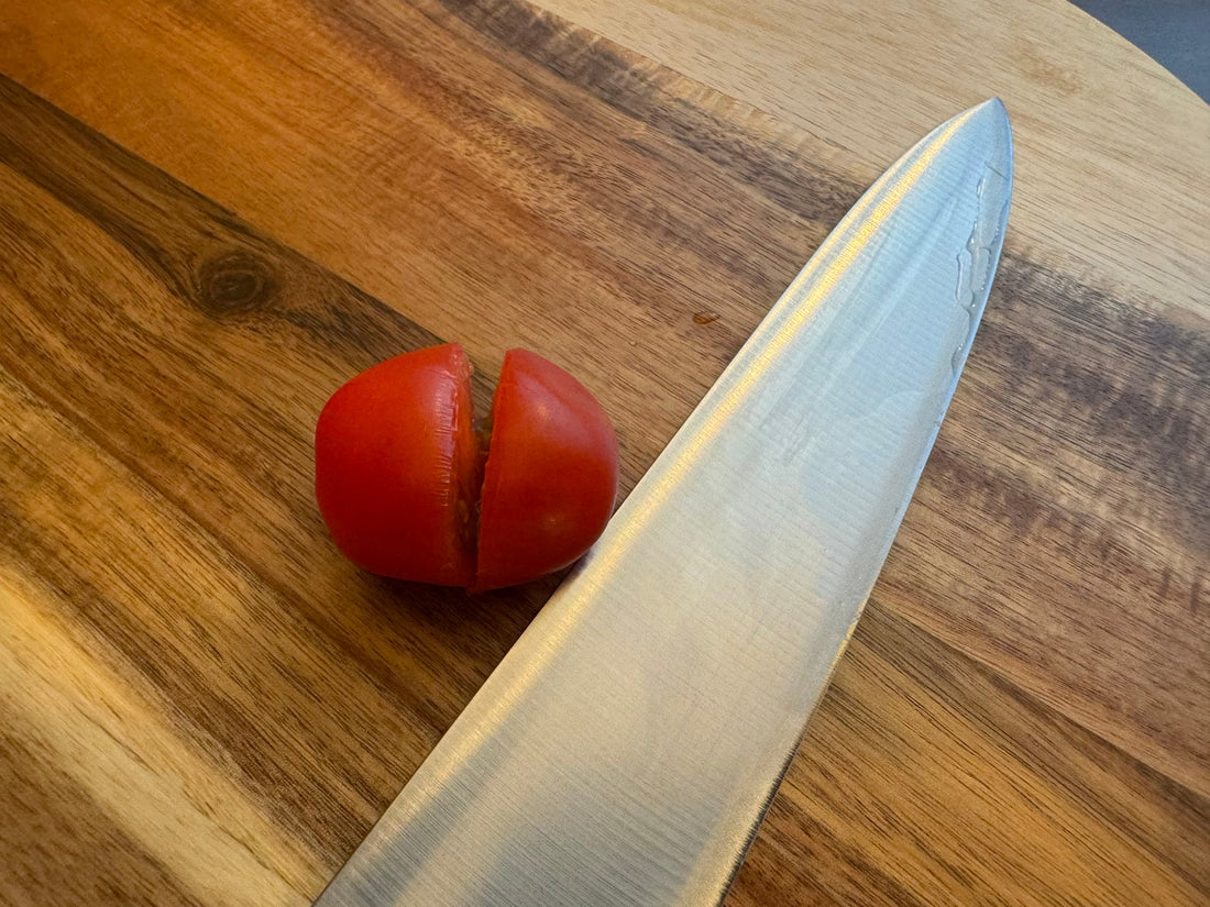 Tomat med oppreven snittflate ved siden av en kjøkkenkniv på en skjærefjøl.